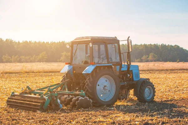 Stora blå traktor plöja upplöjd mark efter skörd av majs gröda på en solig och klar, höst dag. — Stockfoto
