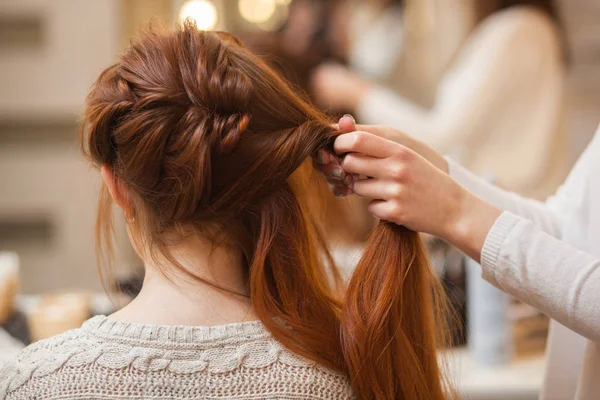 Bella, con lunga, Red-haired ragazza pelosa, parrucchiere tesse una treccia francese, in un salone di bellezza — Foto Stock