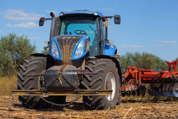 Großer Traktor pflügt das Feld um und entfernt die Überreste der zuvor gemähten Sonnenblume. — Stockfoto