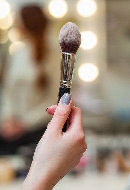 Makyöz elinde bir makyaj fırça tutuyor.