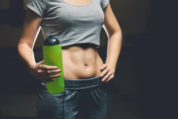Slim girl bodybuilder, holding a bottle of water while exercising in the gym — Stock Photo, Image