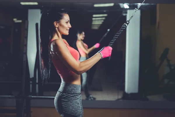 Magro, menina fisiculturista, faz os exercícios de pé na frente do espelho no ginásio — Fotografia de Stock