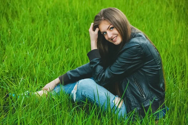 Привлекательная молодая блондинка в сером пальто и джинсах, сидящая на траве — стоковое фото