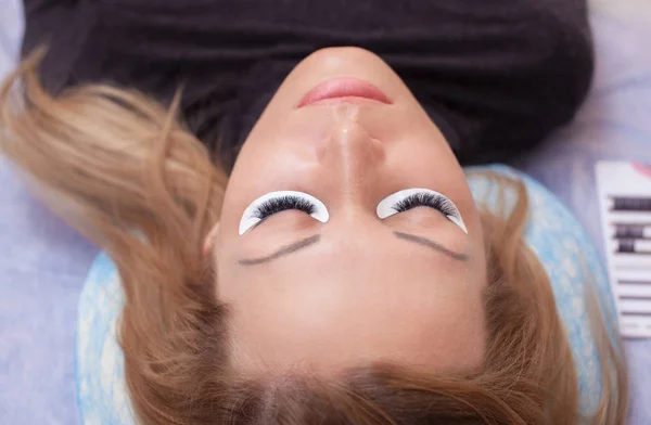 Makeup Master corrects, and strengthens eyelashes beams, holding out a pair of tweezers in a beauty salon — Stock Photo, Image