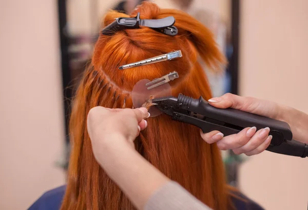 The hairdresser does hair extensions to a young, red-haired girl — Stock Photo, Image