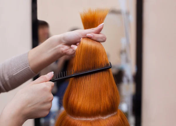 Cabeleireiro pentear seu cabelo longo e vermelho de seu cliente no salão de beleza . — Fotografia de Stock