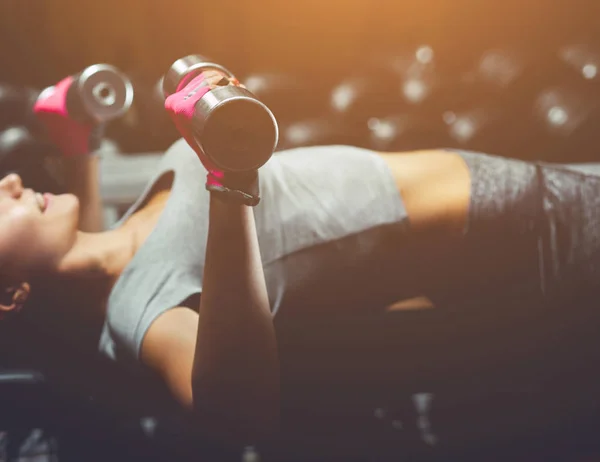 Slim, bodybuilder girl, lifts heavy dumbbell standing in front of the mirror while training in the gym. — Stock Photo, Image