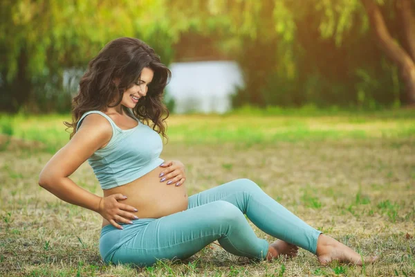 Adult gravid kvinna sitter på gräset i parken — Stockfoto