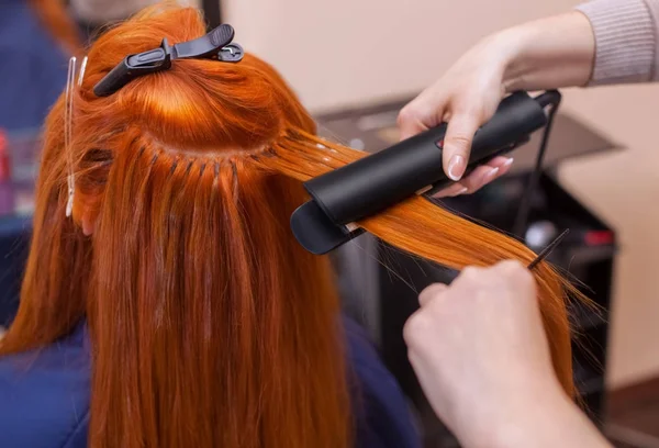 Peluquería hace peinado chica con el pelo largo y rojo en un salón de belleza . — Foto de Stock