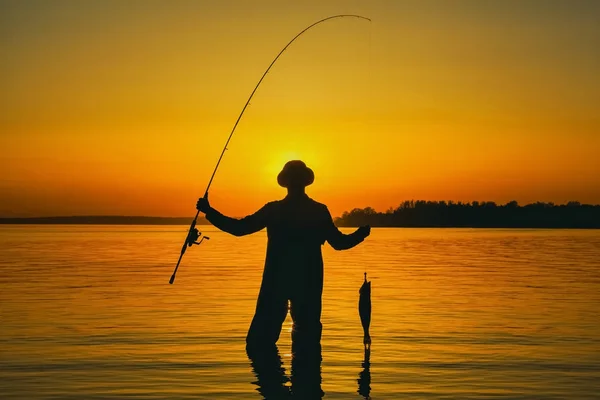 Isherman con una caña de pescar en la mano y un pez atrapado está en el agua — Foto de Stock