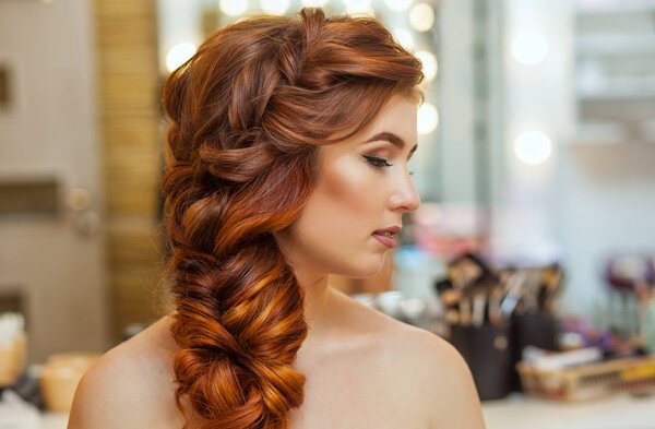 Beautiful, with long, red-haired hairy girl, hairdresser weaves a French braid