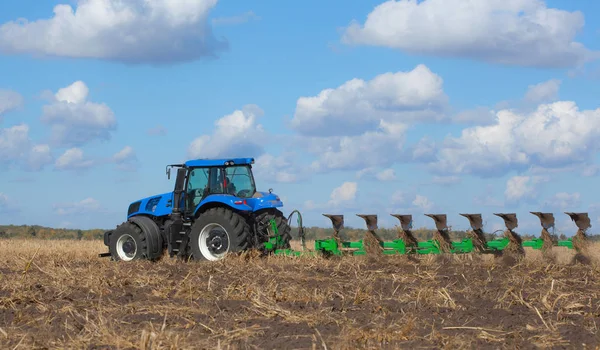 大きな青いトラクター 美しい空を背景にフィールドを耕しします 農業機械の作業 — ストック写真