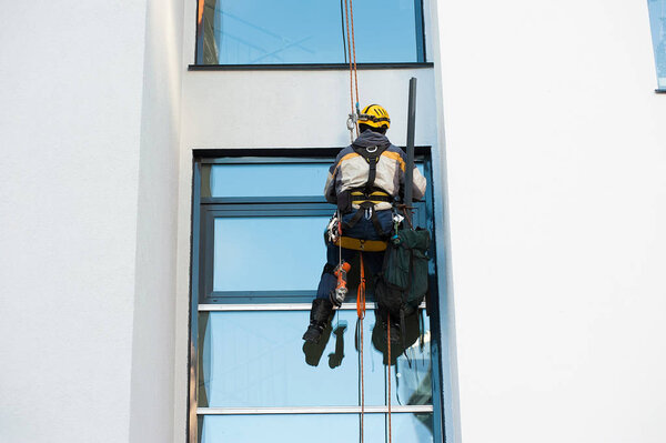 an industrial climber mounts Windows on the colored facade of a new house under construction