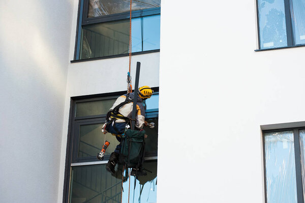an industrial climber mounts Windows on the colored facade of a new house under construction