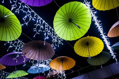 Siyah gökyüzüne karşı dizilmiş renkli şemsiyeler ve çelenkler