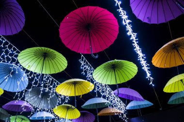 Siyah gökyüzüne karşı dizilmiş renkli şemsiyeler ve çelenkler