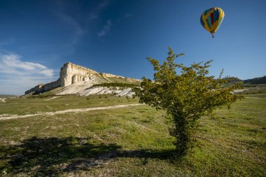 Sıcak hava balonu, sabah bulutlarıyla mavi bir gökyüzünde yerde uçuyor.