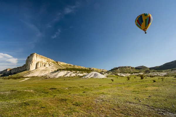 Sıcak hava balonu, sabah bulutlarıyla mavi bir gökyüzünde yerde uçuyor.