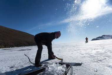 Bir adam kışın donmuş bir gölde baltayla buz keser.