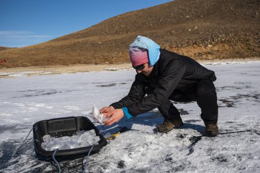 Bir adam kışın donmuş bir gölde baltayla buz keser.