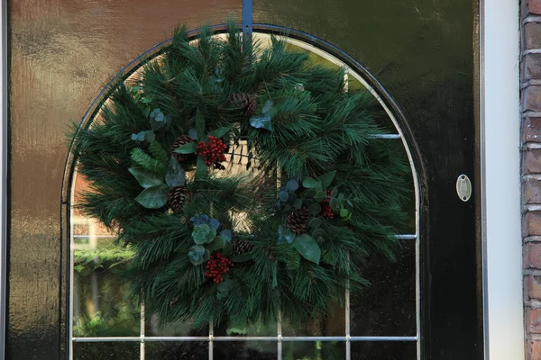 Clásica corona de Navidad con decoraciones en una puerta —  Fotos de Stock