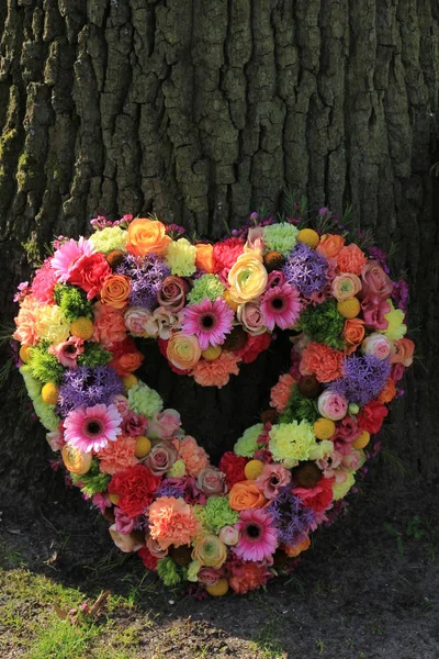 Heartshaped pastel sympathy flowers  or funeral flowers near a tree