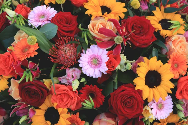 Mixed wedding flower arrangement: big yellow sunflowers with red roses and other flowers in orange and pink