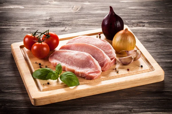 Chuletas de cerdo crudas en tabla de cortar y verduras — Foto de Stock