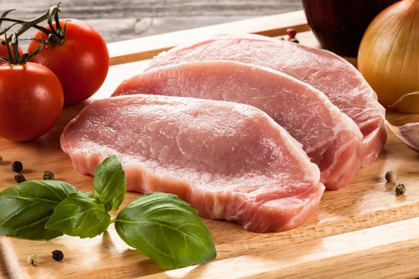 Raw pork chops on cutting board and vegetables — Stock Photo, Image