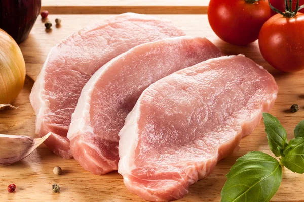 Raw pork chops on cutting board and vegetables — Stock Photo, Image