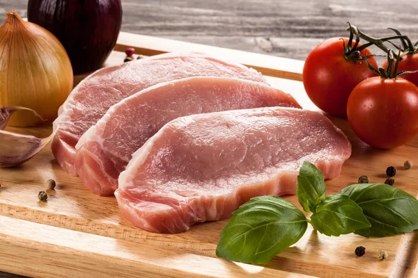 Raw pork chops on cutting board and vegetables — Stock Photo, Image