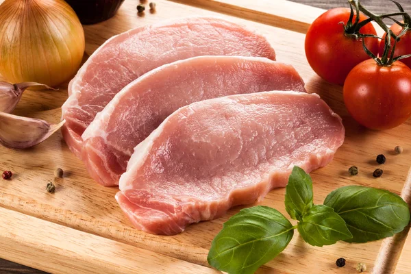 Raw pork chops on cutting board and vegetables — Stock Photo, Image