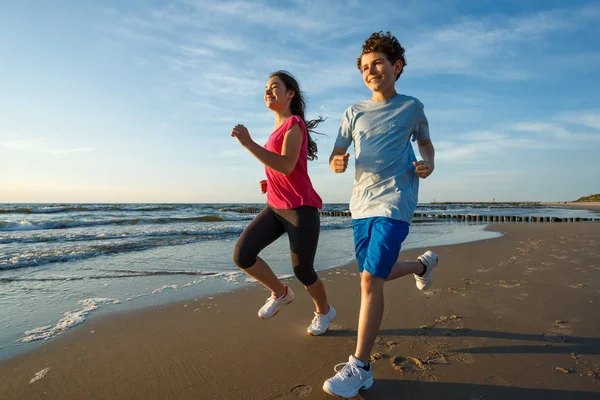 十几岁的女孩和男孩奔跑 跳跃在海滩上 — 图库照片