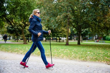 Nordic walking - middle-aged woman working out in city park clipart