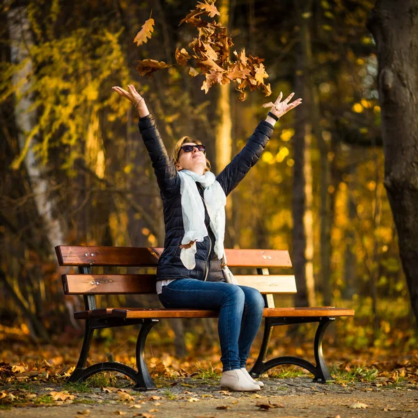 中年の女性は都市公園における葉を投げ — ストック写真