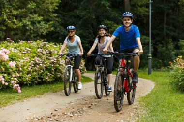 Family of three riding bikes in summer park clipart