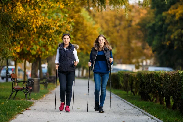 母亲和女儿一起走在秋天的公园里 他们用的是观光棒 北欧漫步 — 图库照片