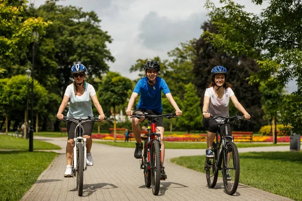 夏の公園でカラフルな花を背景に家族で自転車に乗る — ストック写真