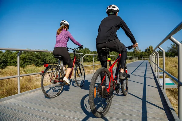 身穿运动服的男女骑着自行车接近河边 — 图库照片