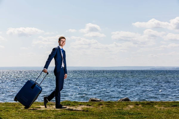 スーツケースを着たビジネスマンが川沿いにポーズ 休暇の概念 — ストック写真