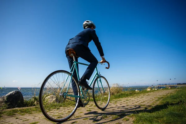 穿着西服 头戴头盔的男子骑着自行车沿着海滨小路走着 — 图库照片
