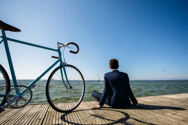スーツを着た男が海辺の自転車で桟橋に座って — ストック写真