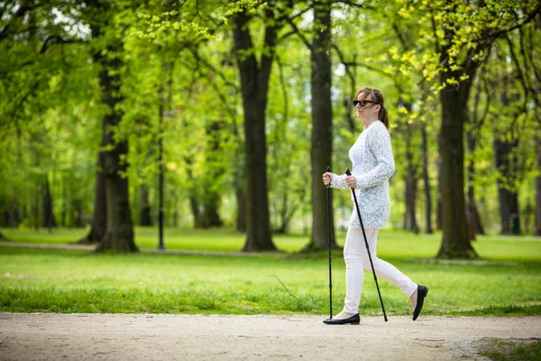 観光を使用して春の公園を歩いて白のカジュアルな服で女性の棒します — ストック写真
