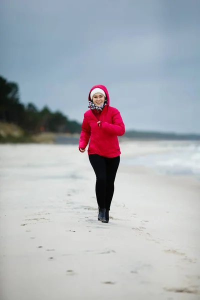 在冬季海滩边奔跑的年轻女子 — 图库照片