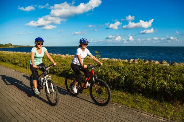 今夏两名身穿运动服的活跃女子在海滨骑自行车 — 图库照片