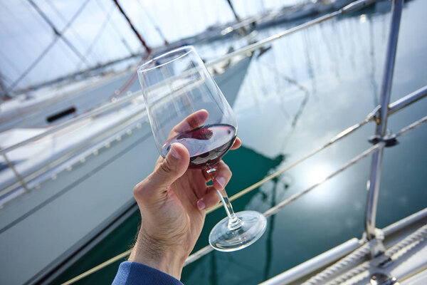 мужчина держит бокал красного вина с яхтой на заднем плане
 
