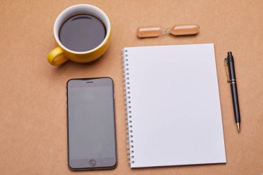 Akıllı telefon ve bir fincan kahve. Masada defter var. Yakın görüş. 