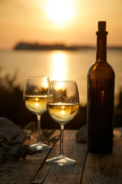 two glasses with wine and bottle with grape during sunset time