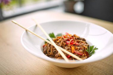 Kızarmış erişteli sobayı beyaz kasede sığır etiyle karıştır, yakın plan. 