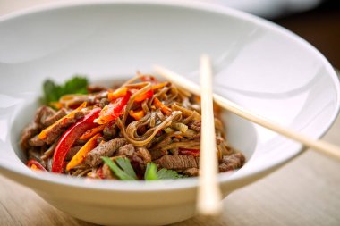 Kızarmış erişteli sobayı beyaz kasede sığır etiyle karıştır, yakın plan. 